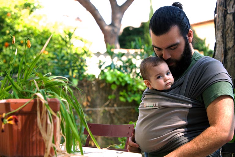 Un papa portant son bébé contre lui dans une écharpe de portage
